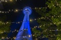 Night scene tall circular tower illuminated blue viewed through strings of decorative fairy lights