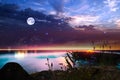 Night at sea starry sky and moon on dramatic clouds sea water wave and stones on horizon blurred city light Royalty Free Stock Photo