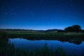 The night sky is illuminated over a small pond, casting a soft glow on the surrounding landscape, Starry night over a peaceful Royalty Free Stock Photo