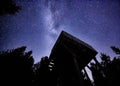 Night sky with the Milky Way over the forest and a bird-watching tower. Trees surrounding the scene Royalty Free Stock Photo