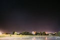 Night Sky Stars Over River Lake Near Houses In Village. Night Starry Sky Above Rural Landscape In Belarus. Glowing Stars