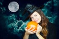 A young cute witch on Halloween with a pumpkin on the background of a creepy dark magical sky. A girl in a witch`s hat hugs a pump Royalty Free Stock Photo