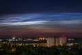 Night sky view of beautiful noctilucent clouds over the city with a cityscape at foreground.