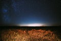 Night Starry Sky Above Field And Yellow City Lights On Background. Night View Of Natural Glowing Stars Royalty Free Stock Photo