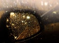 Night street. Side view mirror of motor vehicle covered in raindrops.