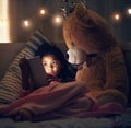 Night, teddy bear and girl with tablet, kid and relaxing with screen light, online reading and social media. Bedroom