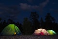 Night tent camp for tourists. Three luminous tents on the background of the forest and dark blue sky. Film noise, grain, high ISO