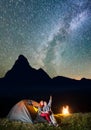 Night tent camping. Romantic couple tourists sitting near tent and campfire and enjoying incredibly beautiful starry sky Royalty Free Stock Photo
