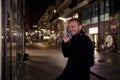 Night time, one young smiling and happy man, 20-29 years, talking over his phone, standing in Autumn coat on street, in business Royalty Free Stock Photo