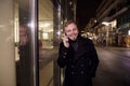 Night time, one young smiling and happy man, 20-29 years, talking over his phone, standing in Autumn coat on street, in front of Royalty Free Stock Photo