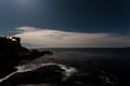 Night time view of a cliffside ocean view with a starry night sky and cirrus cloud and a cruise ship in the distance.