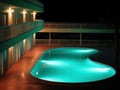 Night view of a hotel and a curved swimming pool with glowing turquoise water. Empt, eerie tropical resort. Generative AI