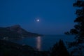 Night view of mount foros in Laspi Bay. A rocky mountain and fool moon above the sea. Moonwalk in the sea.