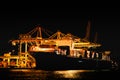 Night view of trieste harbor from the mediterranean sea. disembarkation of a container ship with yellow cranes