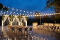 Night wedding ceremony with arch, orchid flowers, chairs and bulb lights in forest outdoors, copy space. Wedding decoration