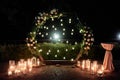 Night wedding ceremony with circle arch, flowers, bulb lights and candles on the backyard outdoors, copy space. Royalty Free Stock Photo