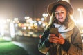 Night. Young woman is standing on city street and is looking at screen of smartphone. Girl uses digital gadget, chatting Royalty Free Stock Photo