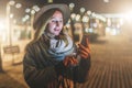 Night. Young woman is standing on city street and is looking at screen of smartphone. Girl uses digital gadget, chatting Royalty Free Stock Photo