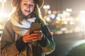 Night. Young woman is standing on city street and is looking at screen of smartphone. Girl uses digital gadget, chatting Royalty Free Stock Photo