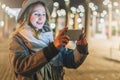 Night. Young woman is standing on city street and is looking at screen of smartphone. Girl uses digital gadget, chatting Royalty Free Stock Photo