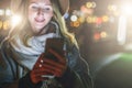 Night. Young woman is standing on city street and is looking at screen of smartphone. Girl uses digital gadget, chatting Royalty Free Stock Photo