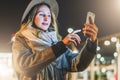 Night. Young woman is standing on city street and is looking at screen of smartphone. Girl uses digital gadget, chatting Royalty Free Stock Photo