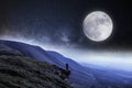 A nightime edit. A hiker on the edge of a cliff surrounded by mountains with the moon and stars above Royalty Free Stock Photo
