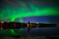 A nightscape view of aurora borealis with a city scape under starry clear sky and reflection from lake water Royalty Free Stock Photo