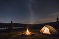 Nighttime camping under stars with glowing campfire and tents in a serene forest setting. Peaceful starry night concept. Royalty Free Stock Photo