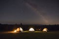 Nighttime camping under stars with glowing campfire and tents in a serene forest setting. Peaceful starry night concept. Royalty Free Stock Photo