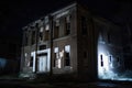 nighttime view of haunted abandoned building, with lights shining through broken windows and doors
