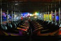 Nighttime view of two colourful rows of Dodgems facing each other.