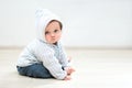 nine month cute baby sitting on floor and looking at camera, baby boy in hoodie at home sitting in front of white wall Royalty Free Stock Photo