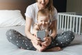 Nine-month-old baby girl sits with her mother and looks on smartphone cartoons. Child is talking to her grandmother via video link Royalty Free Stock Photo