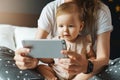 Nine-month-old baby girl sits with her mother and looks on smartphone cartoons. Child is talking to her grandmother via video link Royalty Free Stock Photo