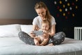 Nine-month-old baby girl sits with her mother and looks on smartphone cartoons. Child is talking to her grandmother via video link