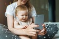 Nine-month-old baby girl sits with her mother and looks on smartphone cartoons. Child is talking to her grandmother via video link Royalty Free Stock Photo