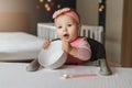 Nine-month-old smiling baby girl sits at white table in highchair and holds empty bowl in her hands, spoon lies on table Royalty Free Stock Photo