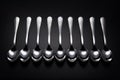 Nine stainless steel spoons on black background.