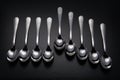 Nine stainless steel spoons on black background.