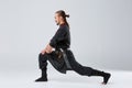 The ninja man pulled his left foot back to stretch the muscles against a gray background