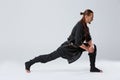 A ninja man pulled his right foot back for stretching muscles against a gray background