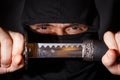 Ninja ready to fight, holding a Japanese sword. Photo of a warrior dressed in black clothes and closed face