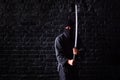 Ninja samurai with katana in attack pose on a dark brick wall background