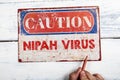 Nipah Virus. Metal CAOTION plate with text on a white wooden background