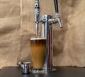Nitrogen infused cold brew coffee next to a nitrogen tap in a tall glass.