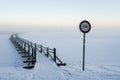 No bicycles road sign next to a snowy wooden boardwalk on a frozen lake, misty winter landscape