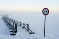 No bicycles road sign next to a snowy wooden boardwalk on a frozen lake, misty winter landscape