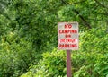 No camping or overnight parking sign with red lettering beside green trees.