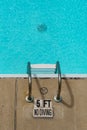 No diving sign by a pool ladder. The water is clear and blue. Depth is marked as 5 feet